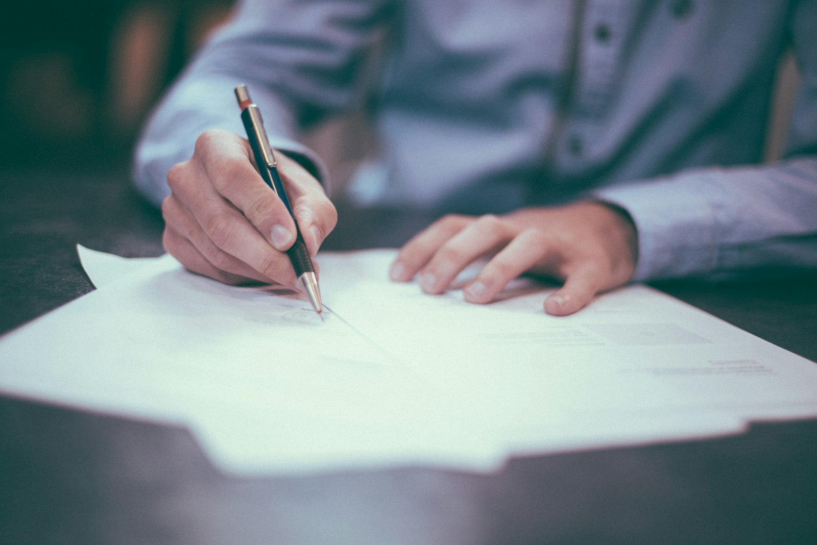 A person in a blue shirt signing a stack of printed documents.