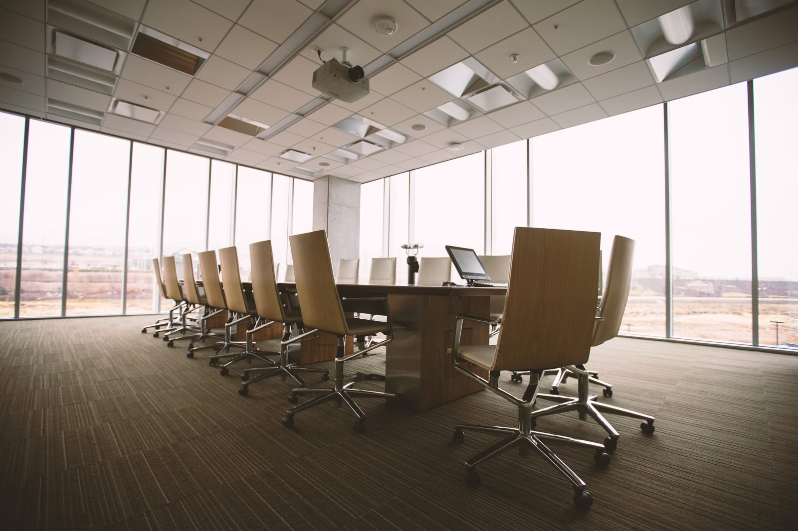 An empty boardroom with a long table and chairs facing a window.