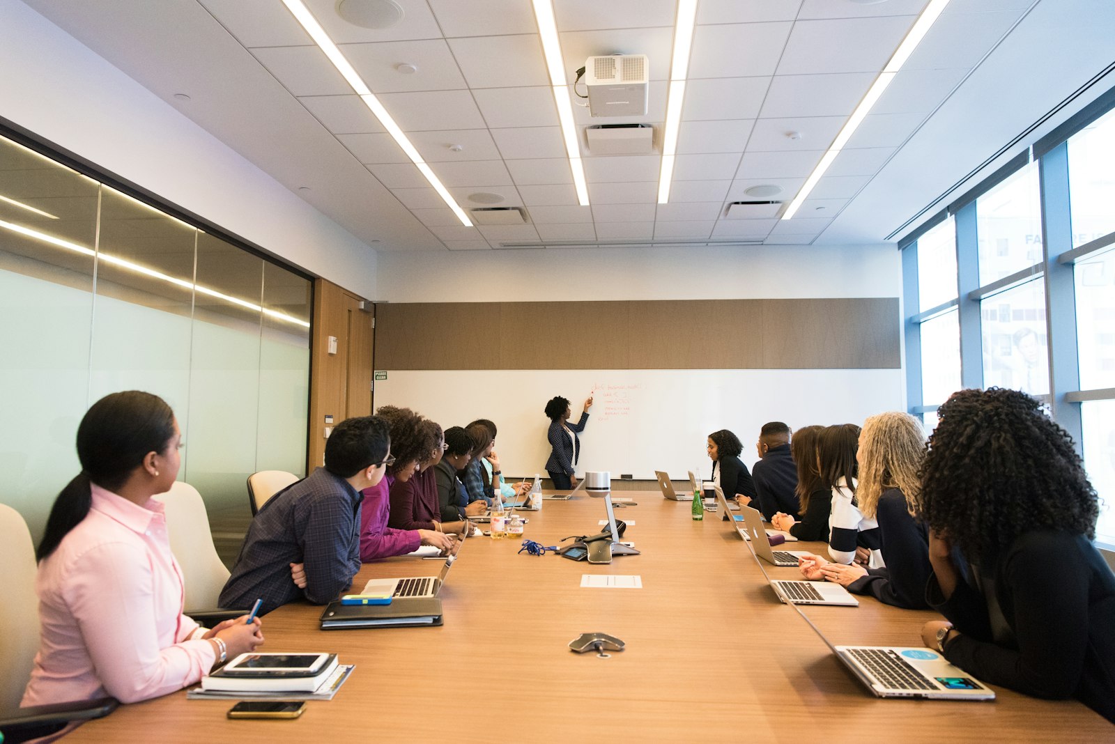 Colleagues around a conference table listening to a presenter in a bright office.