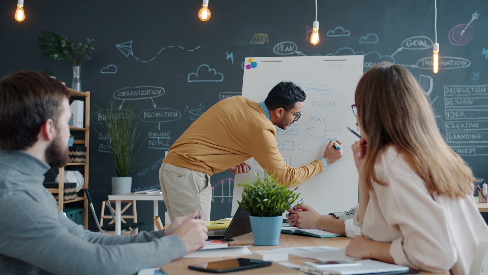 A man presenting at a whiteboard to colleagues seated in a meeting room.