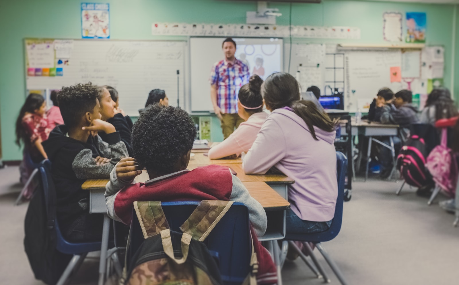 A teacher at the front of a classroom while students work at their desks.