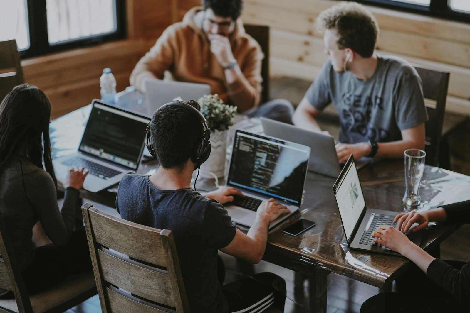 A team working side by side on laptops around a shared wooden table.